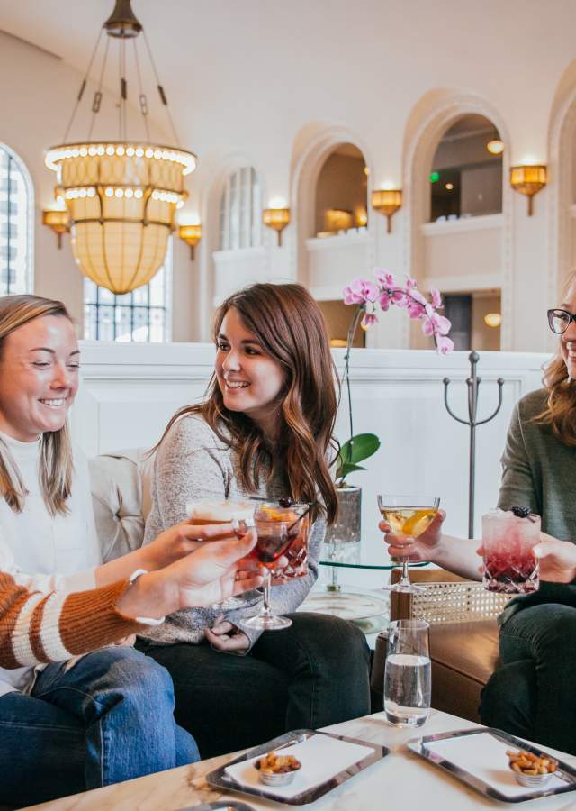 Five women at a table holding up their drinks in Cooper Lounge at Denver Union Station